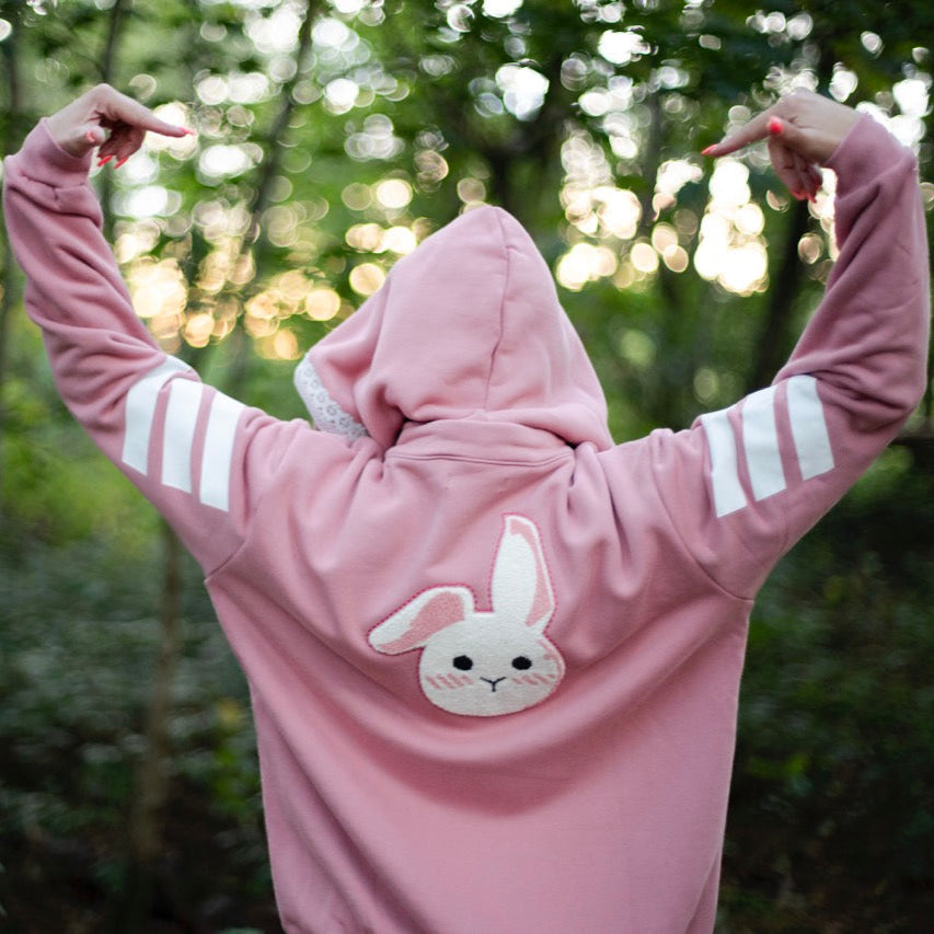 Person wearing a pink hoodie with a bunny design in a forest setting