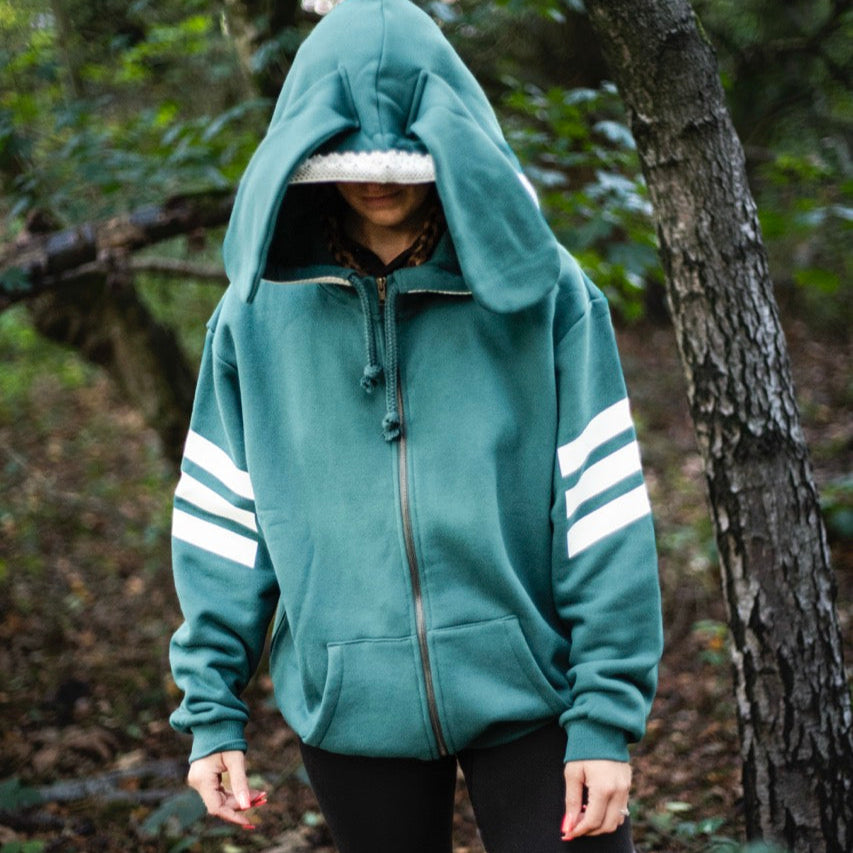 Person wearing a teal hoodie with white stripes in a forest setting